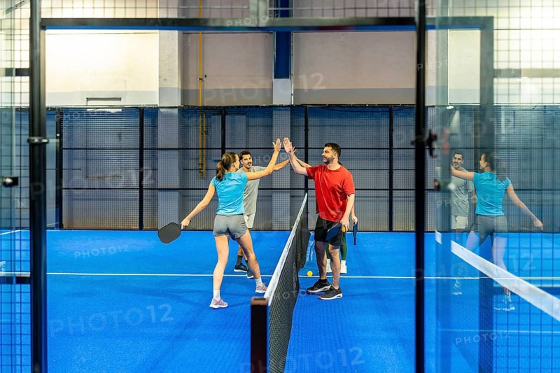 Four enthusiastic players giving high fives after a pickleball match on a bright blue indoor court, showing teamwork, sportsmanship, and enjoying a healthy lifestyle