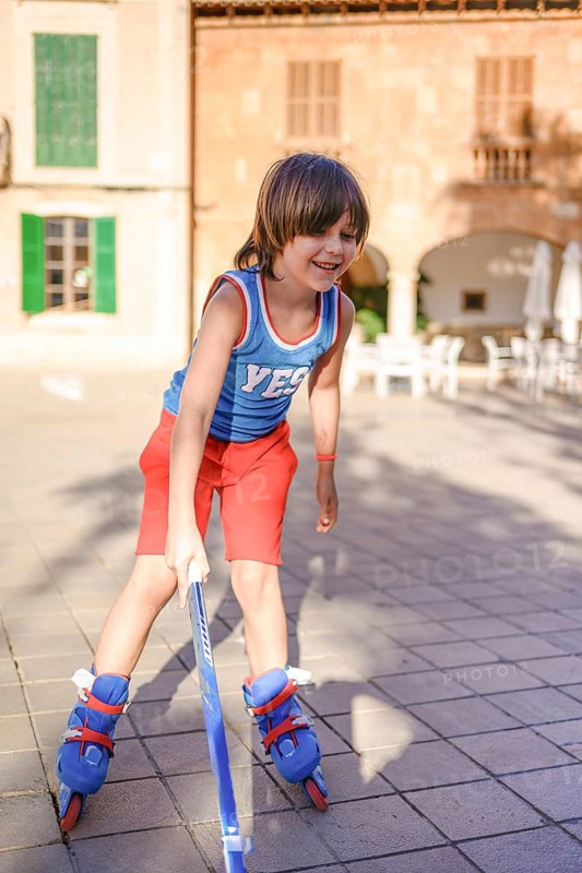 A joyful child roller blades on a sunlit day, using a hockey stick for balance. The scene captures the essence of outdoor fun and playfulness in a vibrant setting