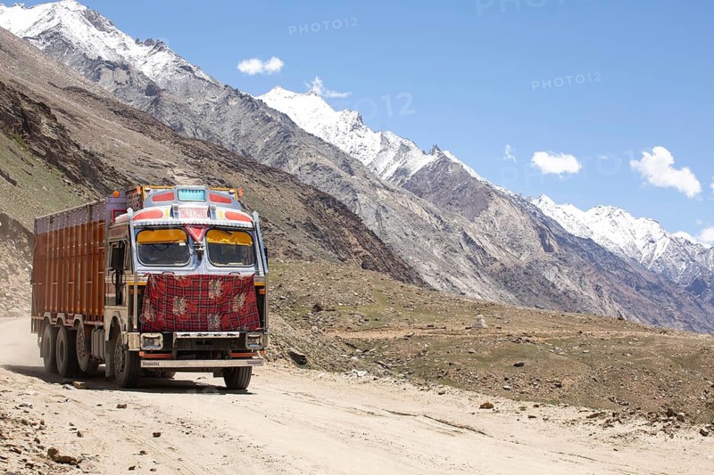 A colorful truck traverses the rugged landscape of Zanskar Valley in Ladakh, India. Snow capped peaks tower in the background, showcasing the region breathtaking natural beauty