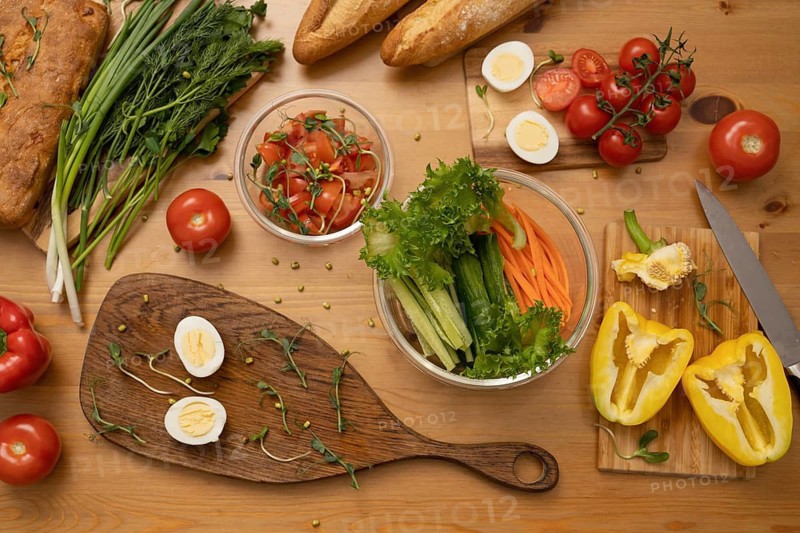 A variety of fresh vegetables, hard-boiled eggs, and whole-grain bread on a wooden table. Ingredients are prepared for a healthy meal. Ideal for culinary or healthy lifestyle themes