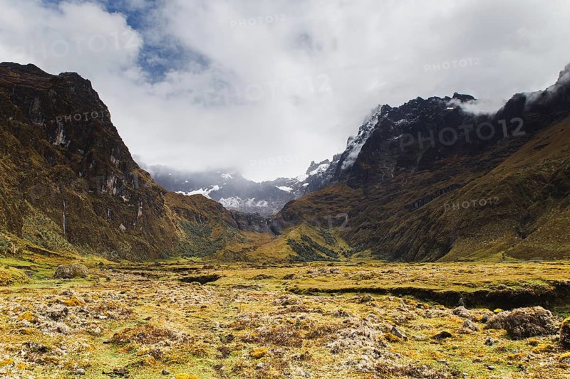 A breathtaking view of the rugged Andean landscape at El Altar volcano, Ecuador, showcasing towering peaks, lush alpine meadows, and misty clouds over rocky slopes