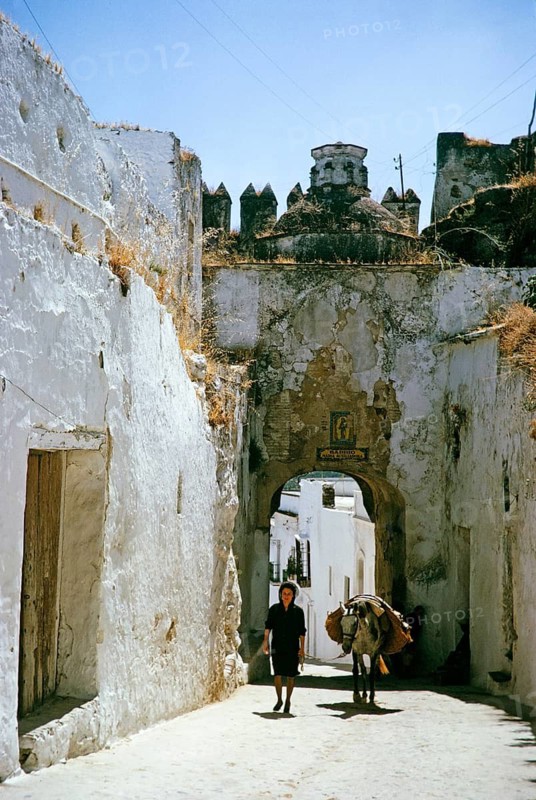 Woman and donkey on a narrow street under an archway, Barrio Maria Auxiladoria, Arcos de la Frontera, Cádiz province, Spain 1964