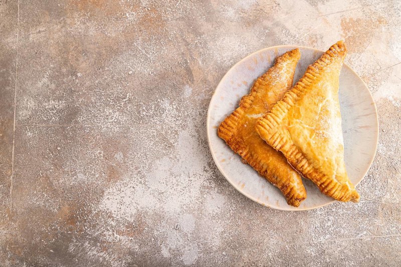 Triangles Pie, Puff Pastry, Samsa with cherry jam on brown concrete background, top view, flat lay, copy space