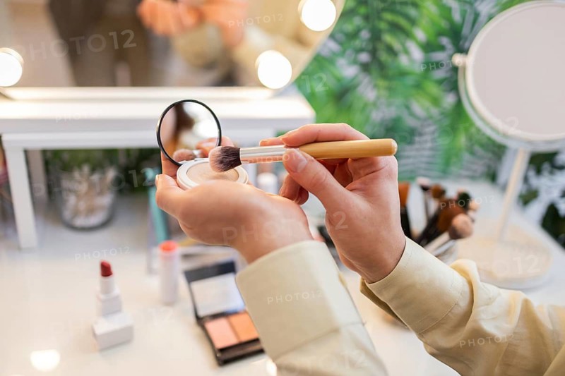 Close-up of hands holding a makeup brush and compact powder while testing organic beauty products in an eco-friendly store The setup features natural cosmetics and sustainable design