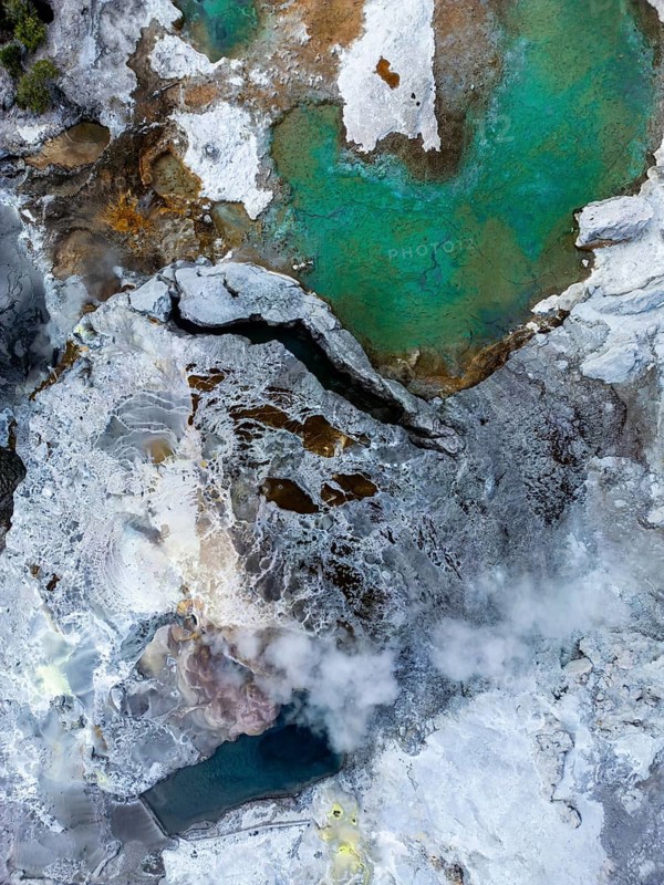 Aerial view showcasing the vibrant hues and dynamic textures of Rotorua's geothermal landscape in New Zealand, highlighting steaming vents and mineral-rich pools