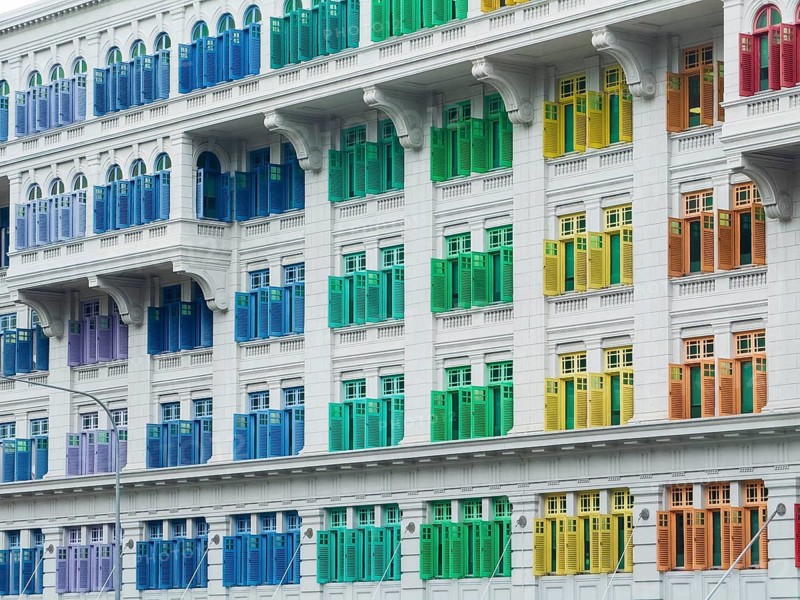 A vibrant facade of a colonial-style building in Singapore, showcasing a row of multicolored shutters in a symmetrical pattern