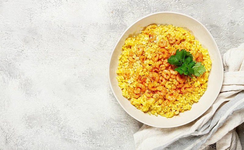 Risotto with shrimp, in a bowl, on a textured surface, with a side dish of fresh coriander, homemade, no people