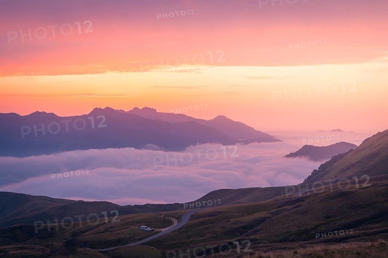 Experience a stunning mountain sunrise as soft pink and orange hues illuminate the sky above rolling hills and valleys, creating a serene and breathtaking landscape in the Pyrenees