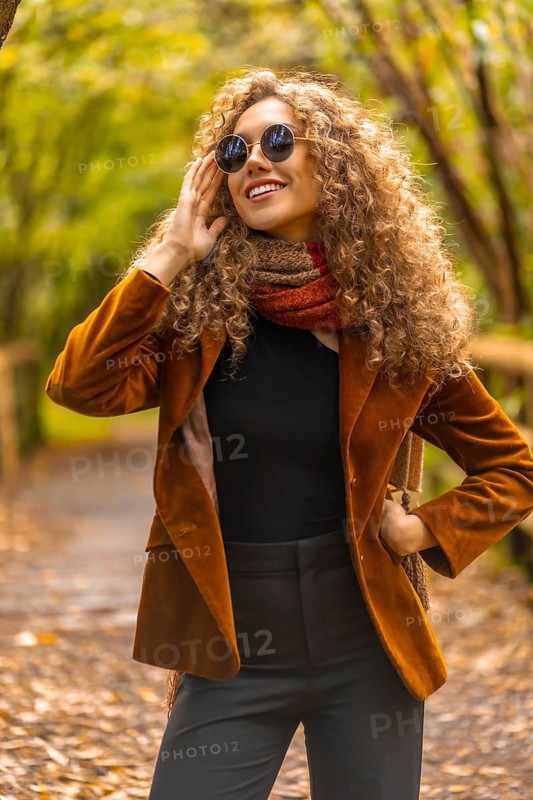 Vertical portrait of a model in sunglasses and casual clothes in a park with fallen leaves in autumn
