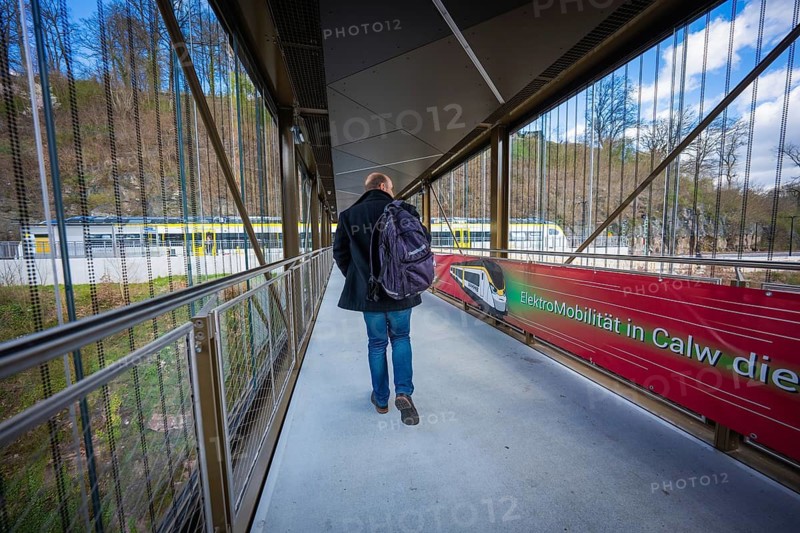 Person walking with backpack across modern bridge next to Zug, Hermann Hesse Bahn, ZOB, Calw, Germany
