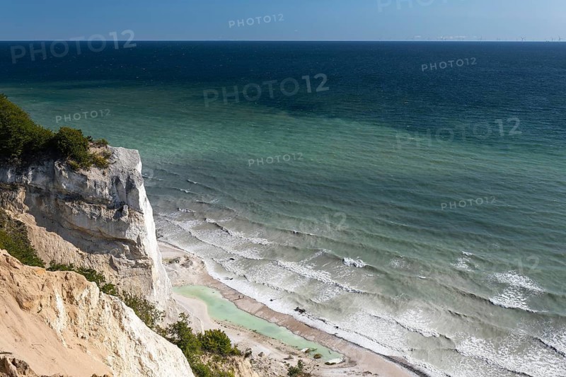 White chalk cliffs in August. People on the beach and by a small lagoon. Milky Baltic Sea under a blue sky. Møns Klint, Sjælland, Denmark
