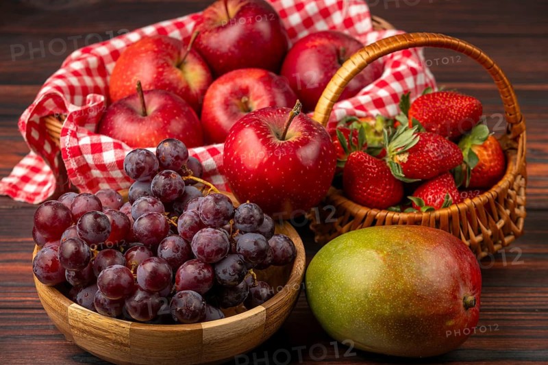 Baskets filled with apples, strawberries, grapes and a mango, arranged on a wooden table