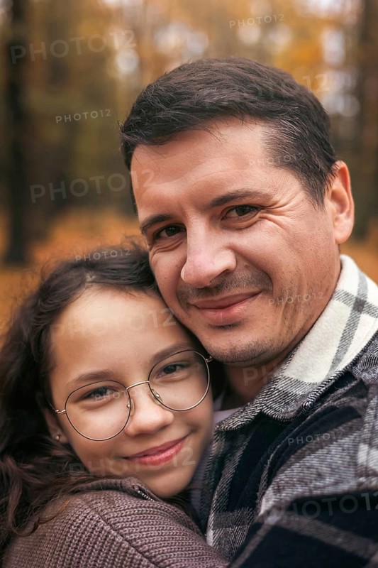 A heartwarming portrait of a father and daughter embracing in a forest during autumn. The warm colors of fall foliage create a cozy atmosphere, highlighting family love and connection