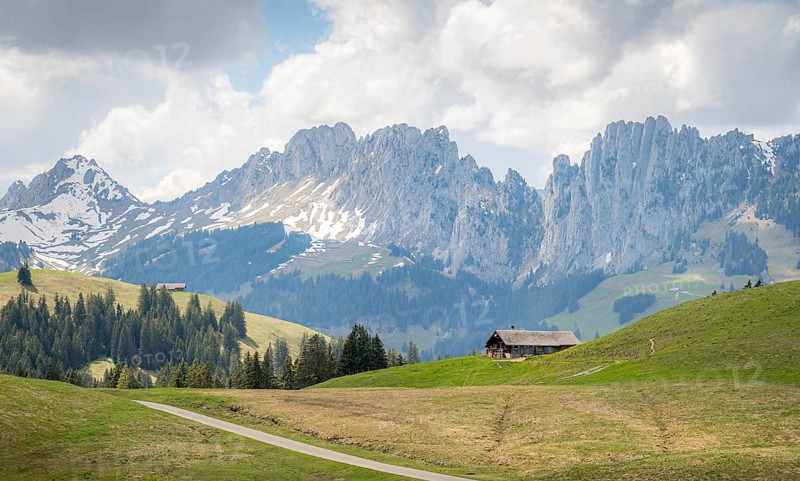 Spring view of a serene landscape in Jaun, Gruyere, featuring the dramatic Gastlosen mountain range and a traditional Swiss chalet nestled among verdant meadows