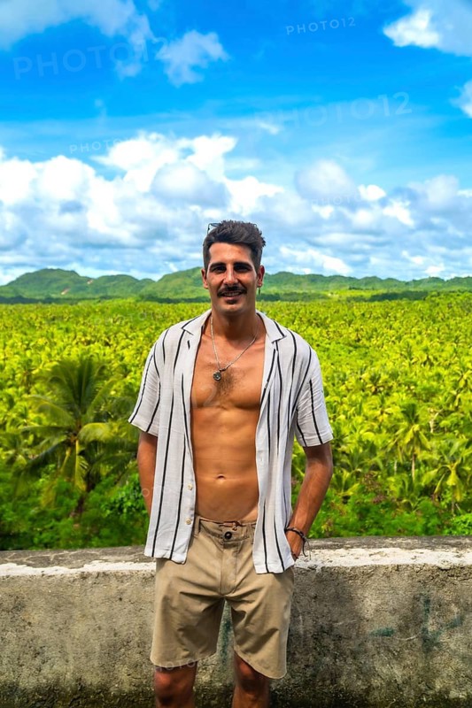 Young man posing in front of a vast coconut plantation in siargao island, philippines, enjoying the tropical landscape