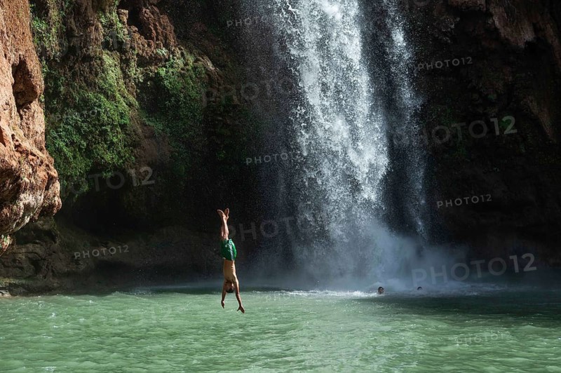 OUZOUD, MOROCCO - OCTOBER 5, 2024: A Moroccan young man jumps headfirst from the high rock into the water under a waterfall Ouzoud