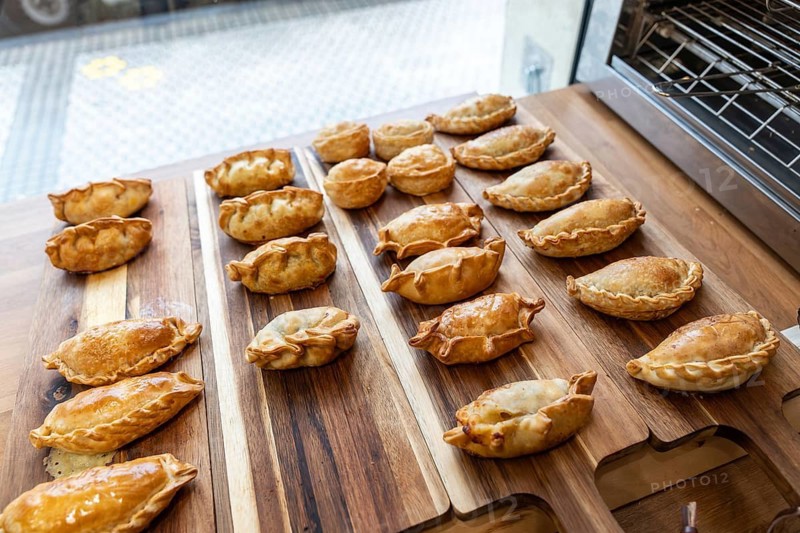 Golden brown empanadas and small round pastries arranged on a natural wood serving board, ready for a savory snack, appetizer, or meal, showcasing baked dough with filling