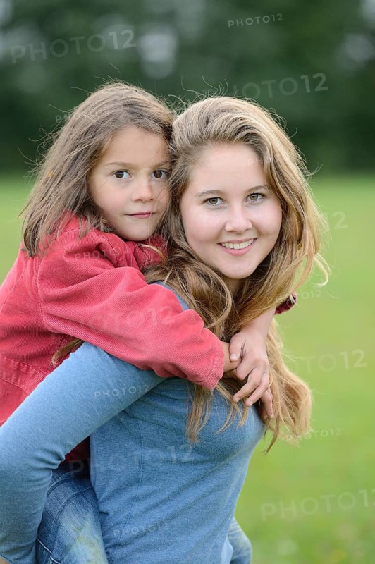 Girl carries her little sister piggyback outdoors, Germany
