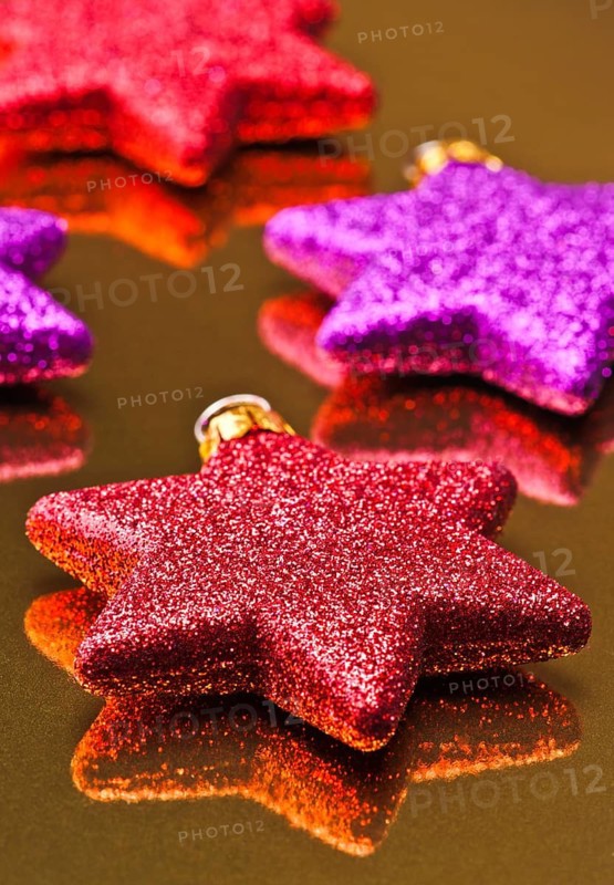 A close-up image featuring a collection of glittering Christmas stars in red and purple shades arranged on a reflective golden surface, perfect for festive season projects
