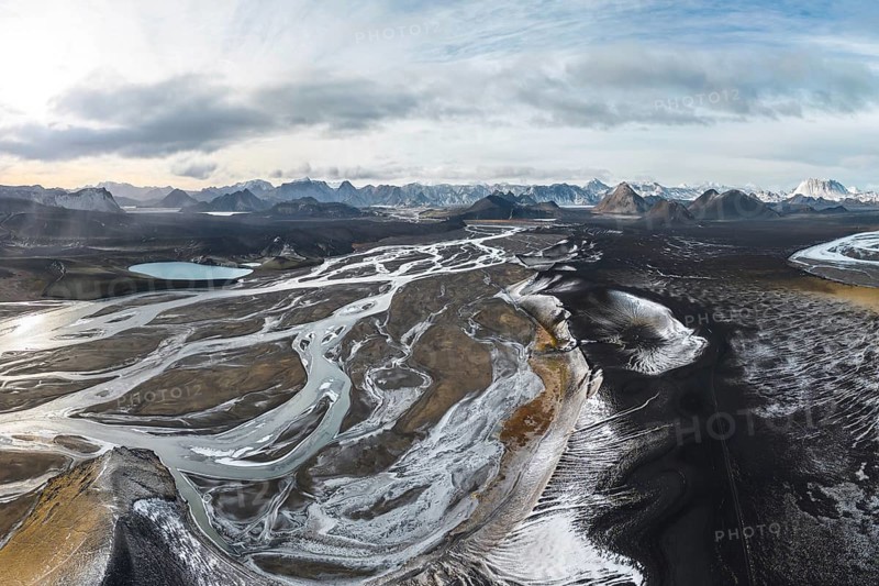 A breathtaking aerial view of Iceland's Highlands, showcasing rugged terrain, winding rivers, and snow-dusted landscapes under a vast, cloudy sky
