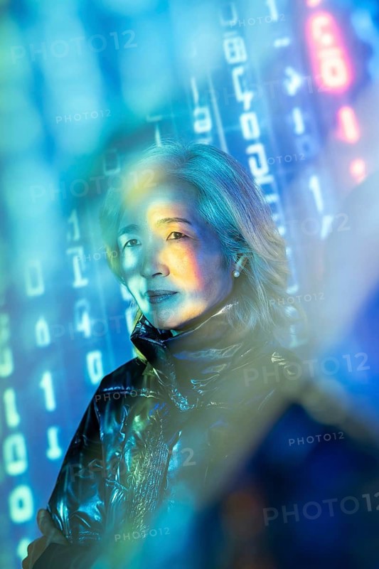An elderly Asian woman experiences the intersection of reality and virtual worlds in the metaverse. Surrounded by digital elements, she explores new technology horizons