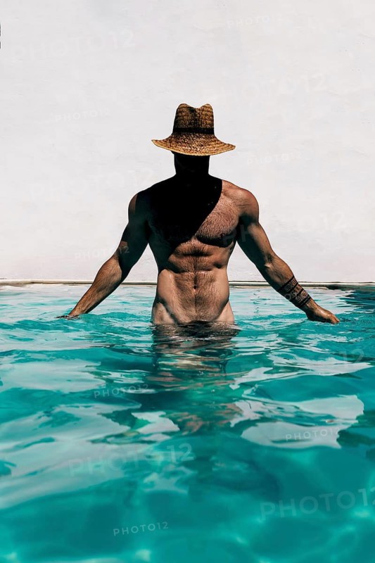Unrecognizable fit man wearing a hat, standing in a swimming pool naked, with toned muscles visible, representing summer relaxation and anonymity