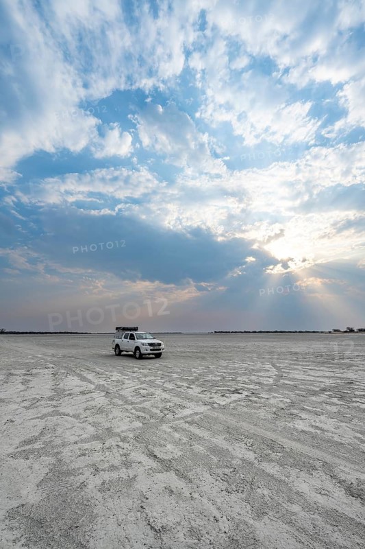 Toyota Hilux off-road vehicle on a salt pan, dramatic clouds with sunbeams, wide open plain, Nxai Pan National Park, Botswana