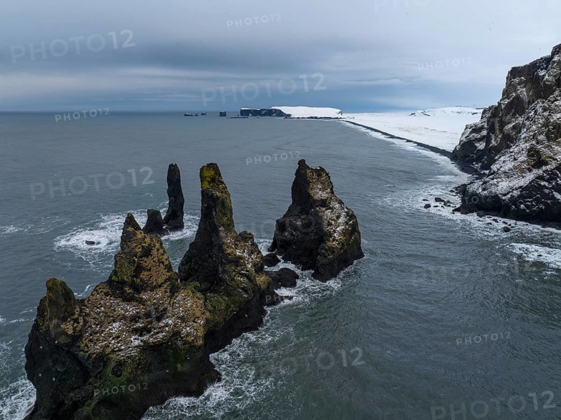 Captivating image of Vik's snow-covered coastline featuring striking sea stacks protruding from the ocean, against a moody winter sky in Iceland's dramatic landscape