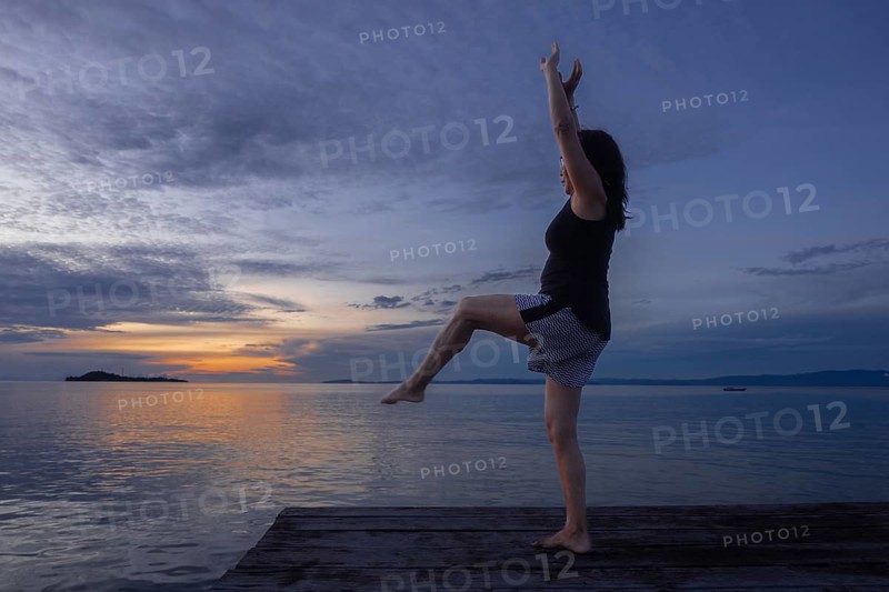 A tourist practices yoga at sunset on a wooden pier, surrounded by the serene waters of Waigeo Island, part of the stunning Raja Ampat Archipelago in West Papua, Indonesia