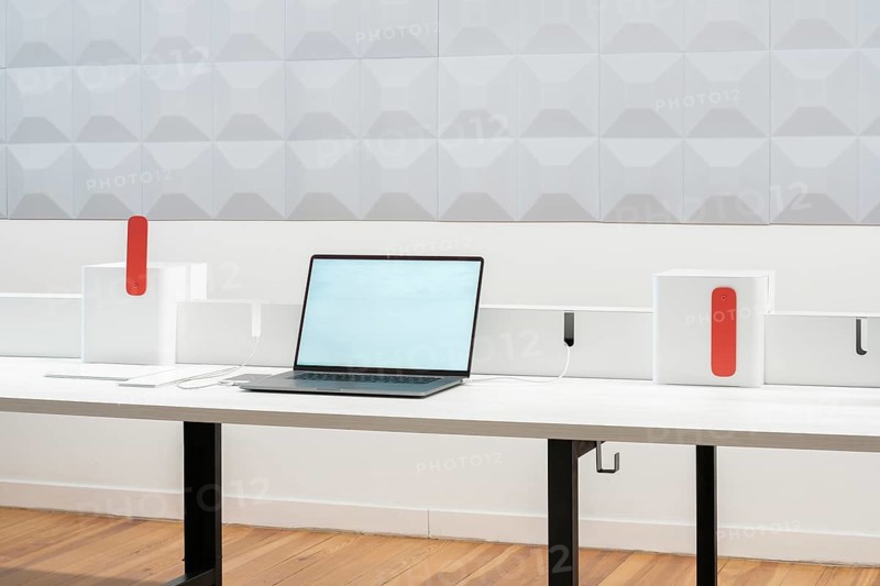 A modern office workspace featuring a laptop on a sleek desk with minimalistic design elements. The backdrop includes geometric wall patterns and stylish organizers