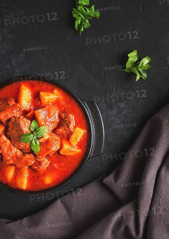 Stew with potatoes, in tomato sauce, with spices and herbs, close-up, no people, on a black background