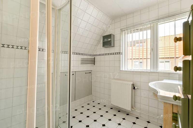 A bright, modern bathroom featuring elegant tile work, a shower area, and a well-lit window. The minimalist design creates a spacious atmosphere