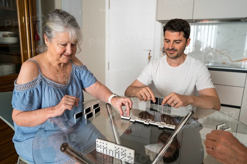A joyful multigenerational family gathered around the kitchen table, engrossed in a lively game of dominoes, highlighting the bonds of shared fun and companionship