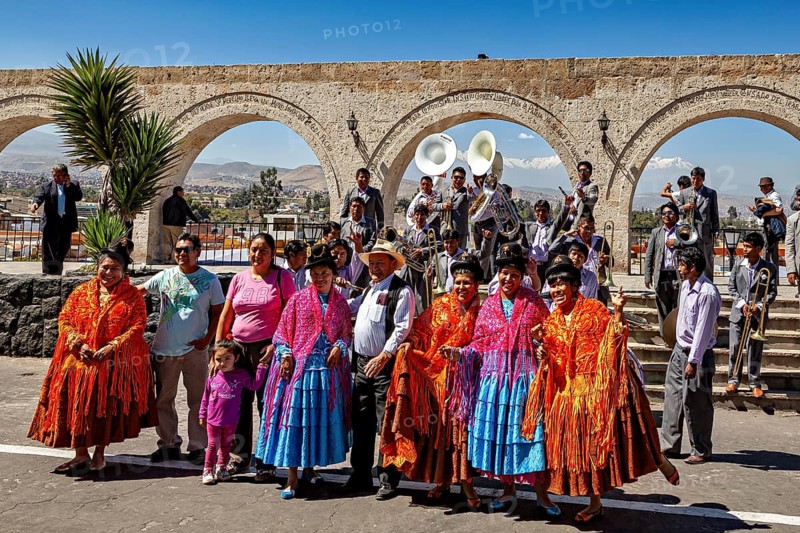 A group of people in traditional colorful clothes with a wind band and bows in the background, a colorful dance and folklore group in Arequipa in Peru