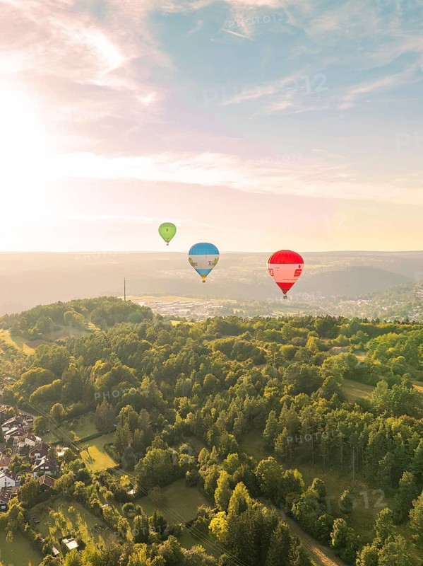 Hot air balloons flying over wooded hills in a landscape at sunset, Calw, Black Forest, Germany