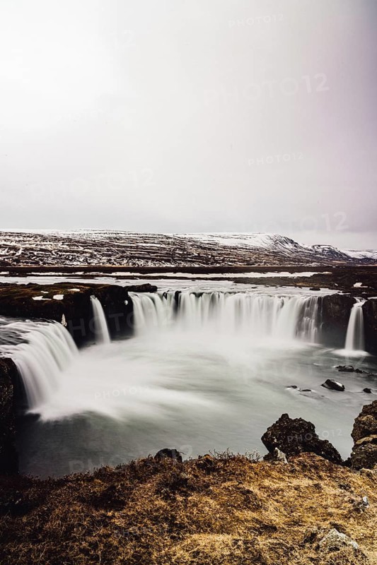 Discover the serene beauty of Godafoss Waterfall in Iceland, where cascading waters flow gracefully over rocky cliffs, surrounded by a striking winter landscape
