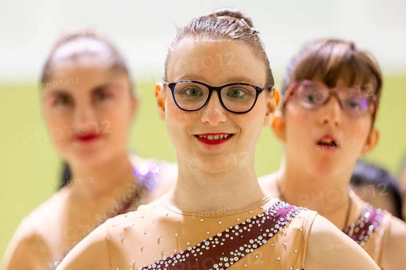 A group of diverse young gymnastic in sparkling costumes, ready for a performance. They exude confidence and joy as they smile, with one in focus, showcasing teamwork