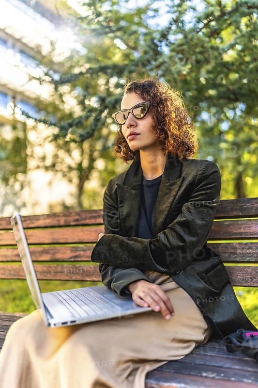 Vertical photo of an Arab young beauty student using laptop sitting on park bench