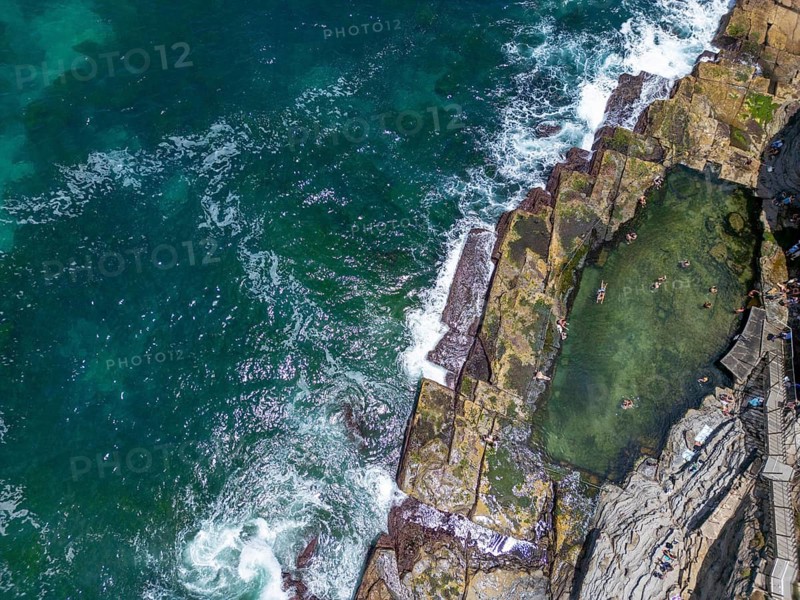 Aerial view of a striking ocean pool nestled among rugged rocks in New South Wales, Australia. Crystal-clear waters contrast with the vibrant turquoise sea. Relaxing coastal scene