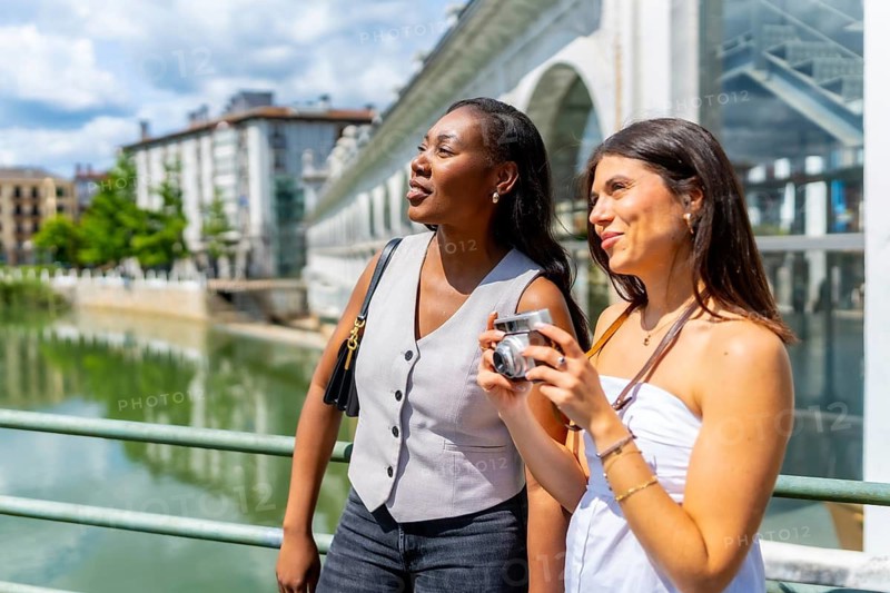 Two women enjoying sightseeing in turin, taking photos with a vintage camera near valentino park, exploring italian culture by the po river