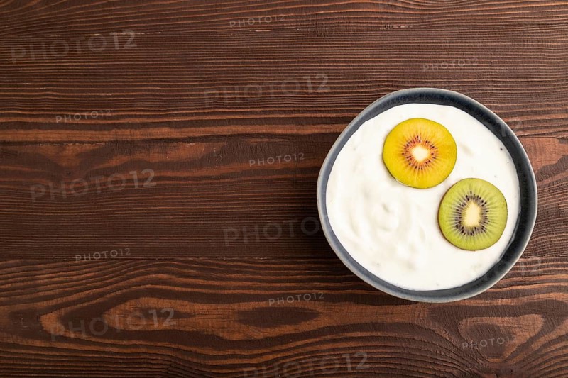 Yogurt, with kiwi in blue bowl on brown wooden background, top view, flat lay, copy space, minimalism