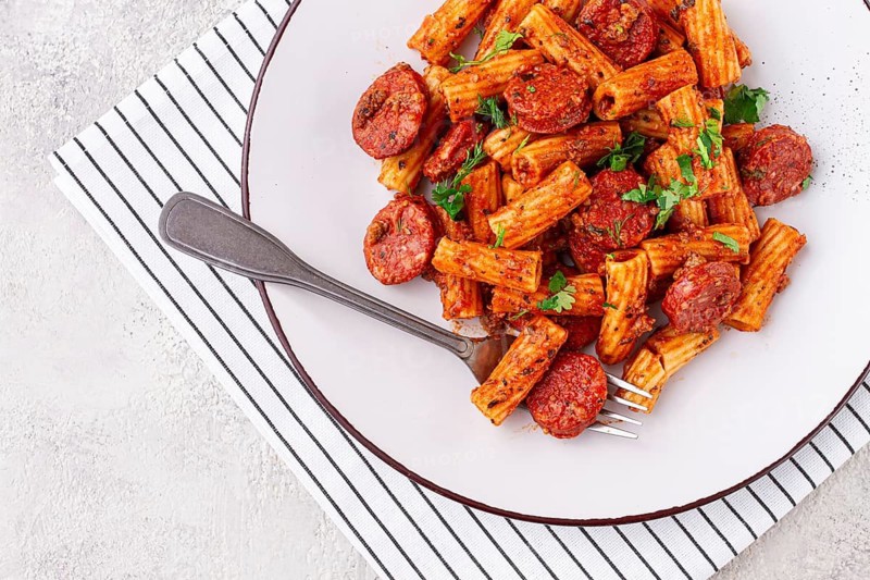 Rigatoni pasta with spicy sausage, and rich tomato sauce served, on a white plate, homemade