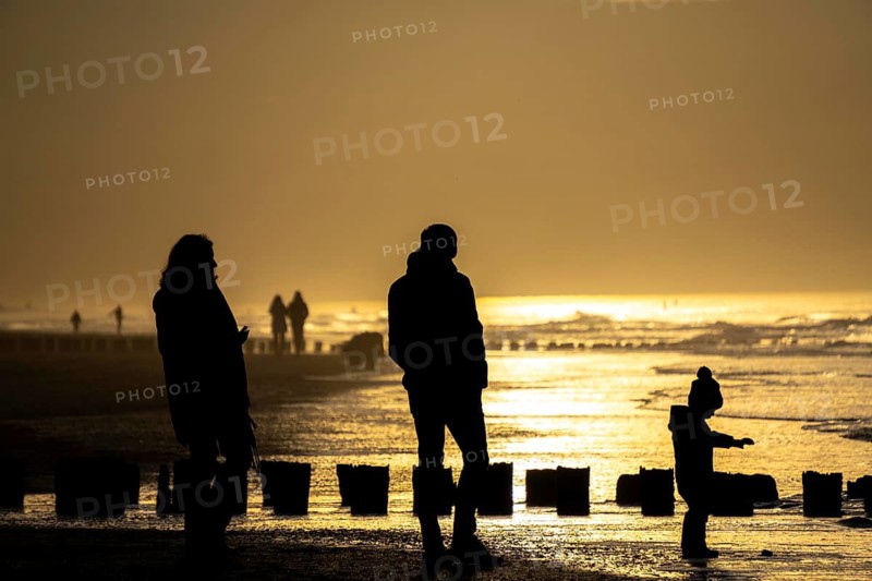 Winter on the North Sea, sunset at sea, beach walkers, coastal protection, through wooden posts, paalhoofden, on the beach, breakwater, the piles rammed into the sandy soil in double rows slow down the waves and ocean currents and thus slow down the flow rate of seawater, so less sand is washed away from the standing position, near Domburg, Walcheren peninsula in the Dutch province of Zeeland