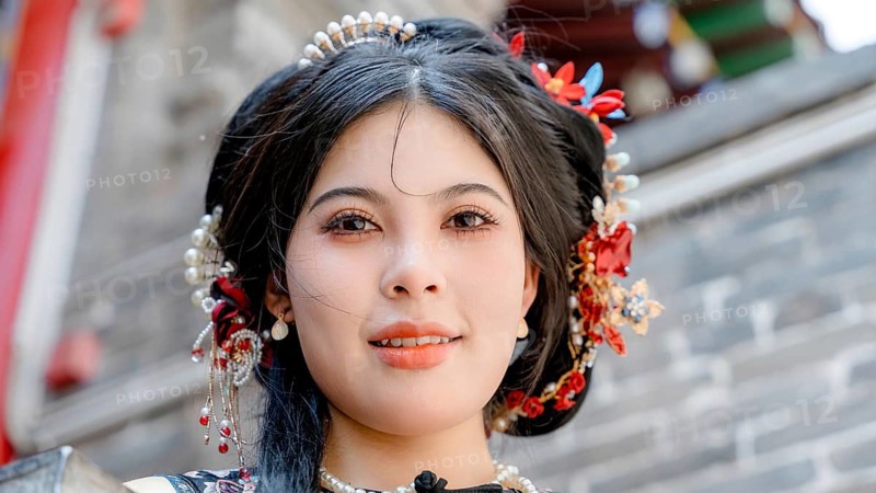 A woman dressed in traditional Qing dynasty clothing looks at the camera in Pingyao, China. Her elaborate headdress and ornate outfit reflect historical elegance