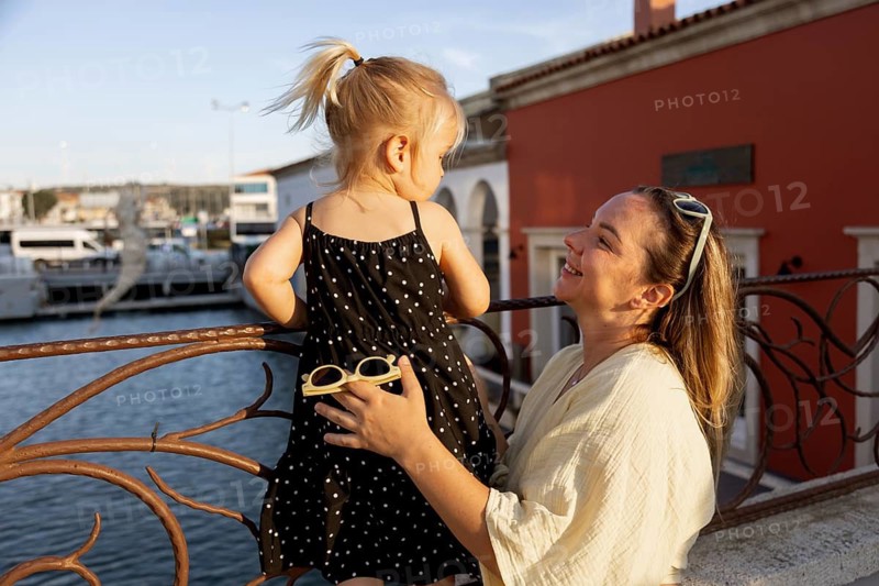 A joyful mother admires her young daughter as they spend time together outdoors. The serene setting and warm sunlight highlight their loving bond and happy expressions