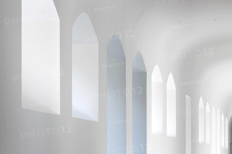 A serene view of arched windows in a minimalist white interior of a hospital. The soft lighting and clean design create a peaceful, airy atmosphere, highlighting architectural elegance