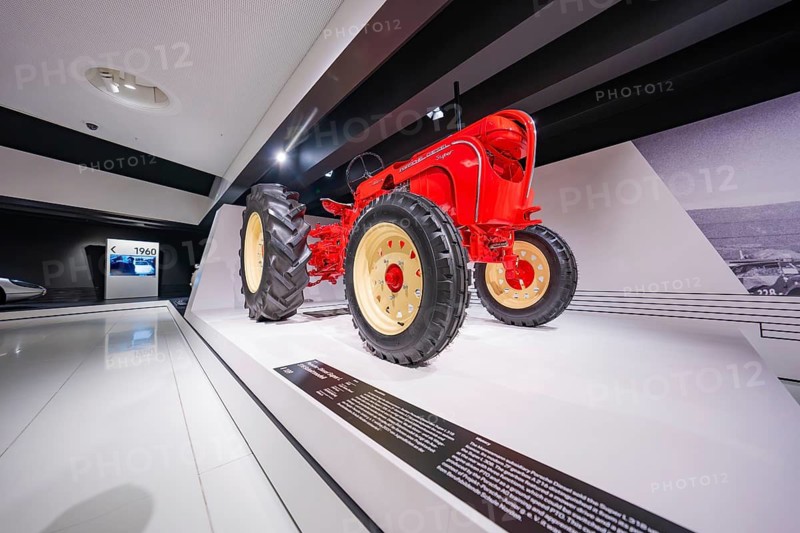 Side perspective of a red tractor in a modern exhibition hall, Porsche Museum, Stuttgart, Germany