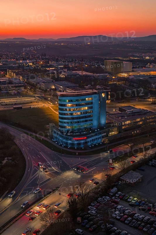 An illuminated high-rise building in the city at dusk with an orange sky, Porsche, Bietigheim, Germany