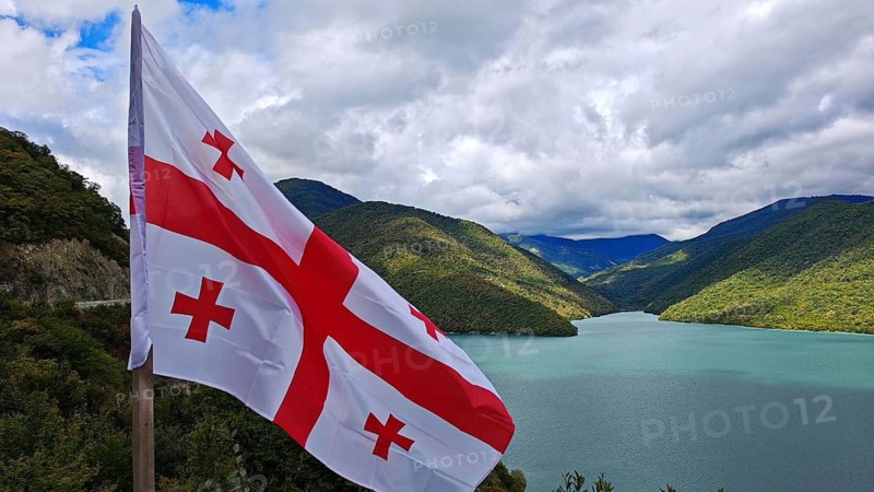 Georgian flag waving against a landscape of lakes and mountains, Georgia