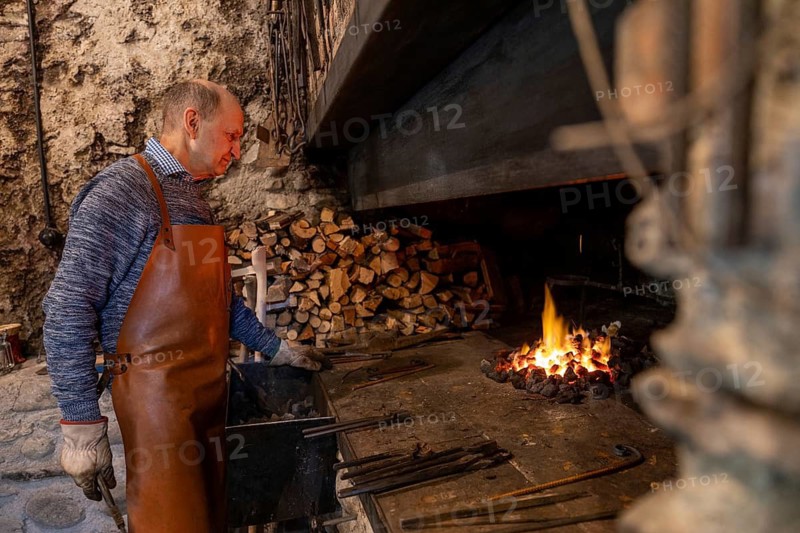An elderly blacksmith works diligently in his Salzburg workshop, skillfully preserving centuries-old traditions of blacksmithing in the heart of Austria